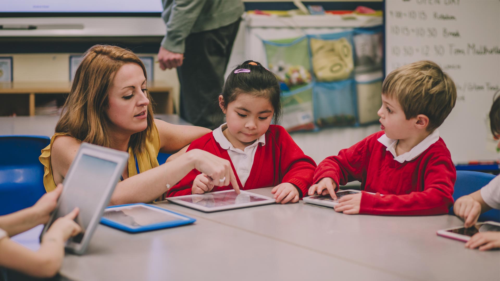 A teacher helping a young primary-aged child use a tablet.