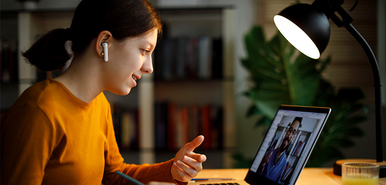 Woman sitting at a table with a lamp and talking to a teacher on her laptop online