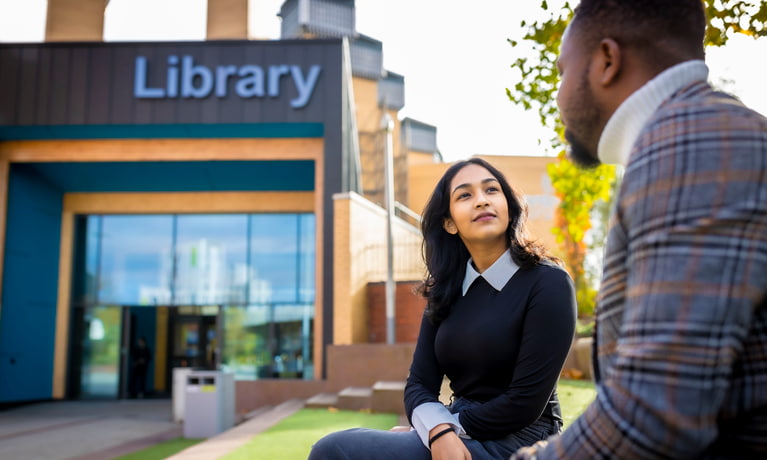 Two students sat in front of the library talking