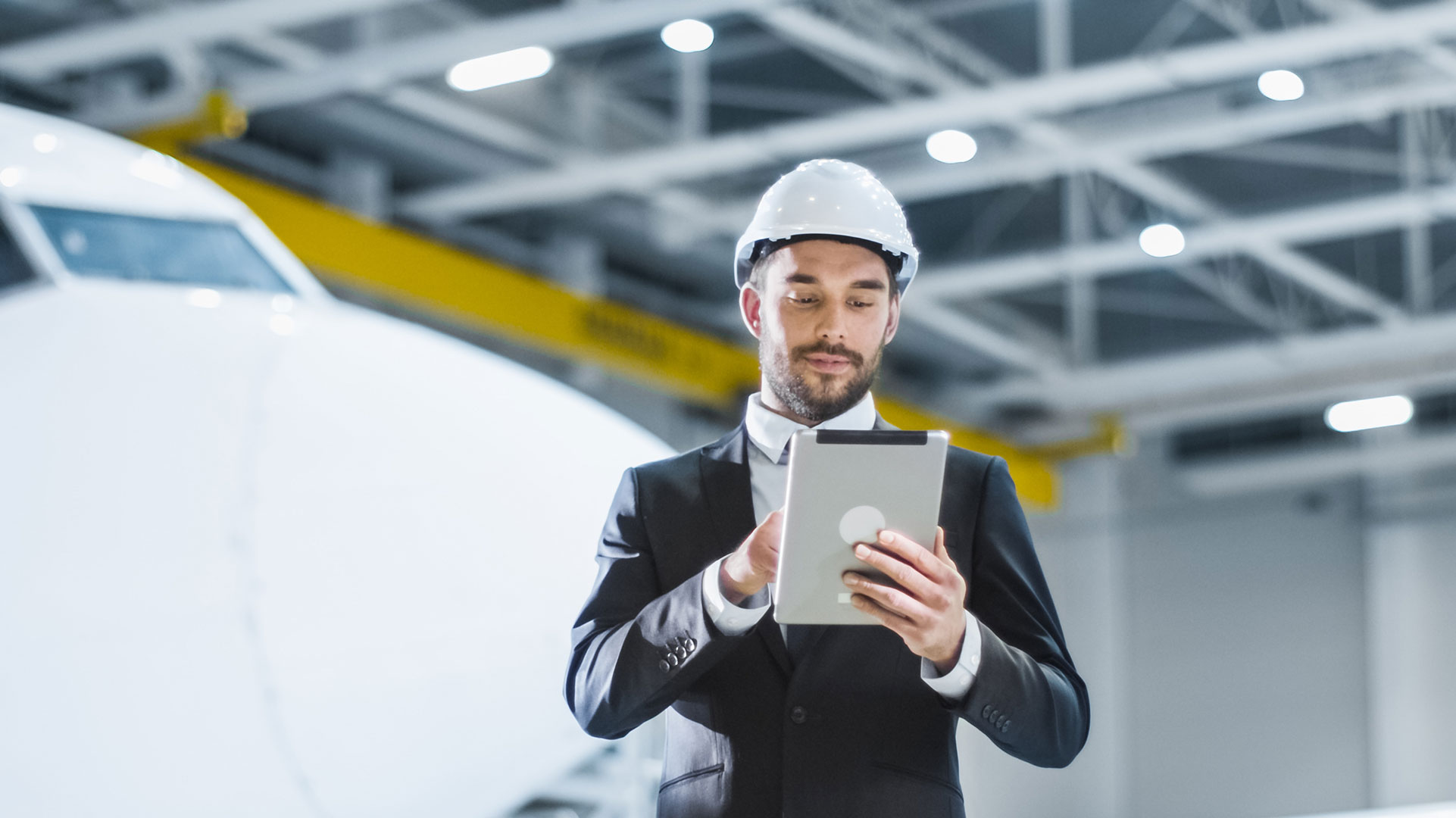 Aviation Management student in an airport hangar, using a tablet, in front of a plane