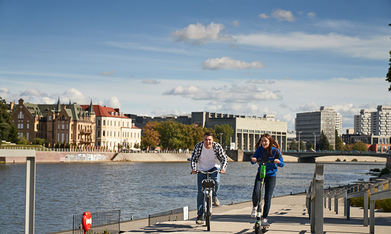 Two people riding their bikes along the river bank